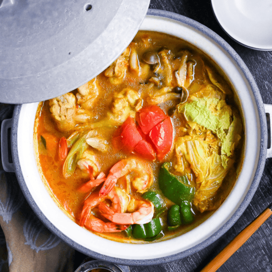 Japanese Curry Hot Pot (Kare Nabe) with chicken, prawns, vegetables and cheese in a gray ceramic pot on a black wood-effect background top down