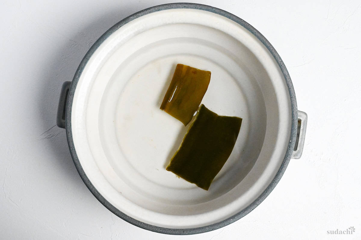 two pieces of kombu (dried kelp) in a pot of water on a white background