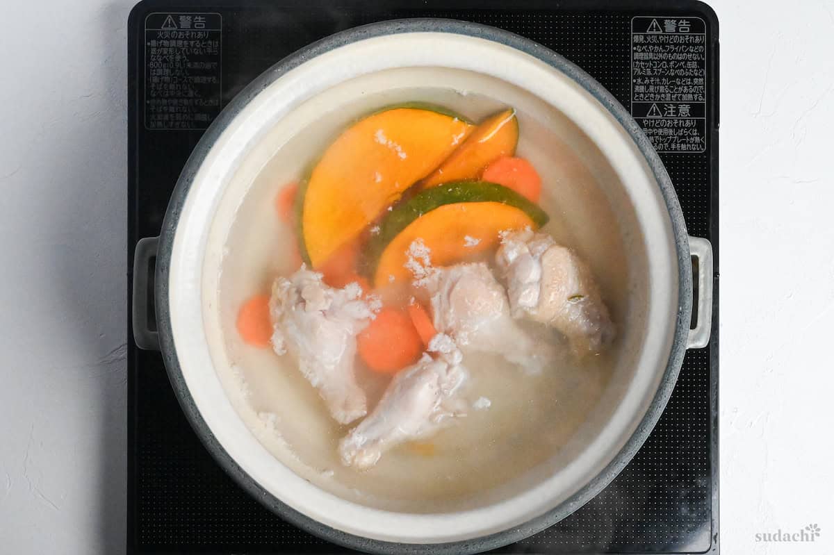 chicken, carrots and kabocha simmered in kombu dashi in a gray ceramic pot on a black stove