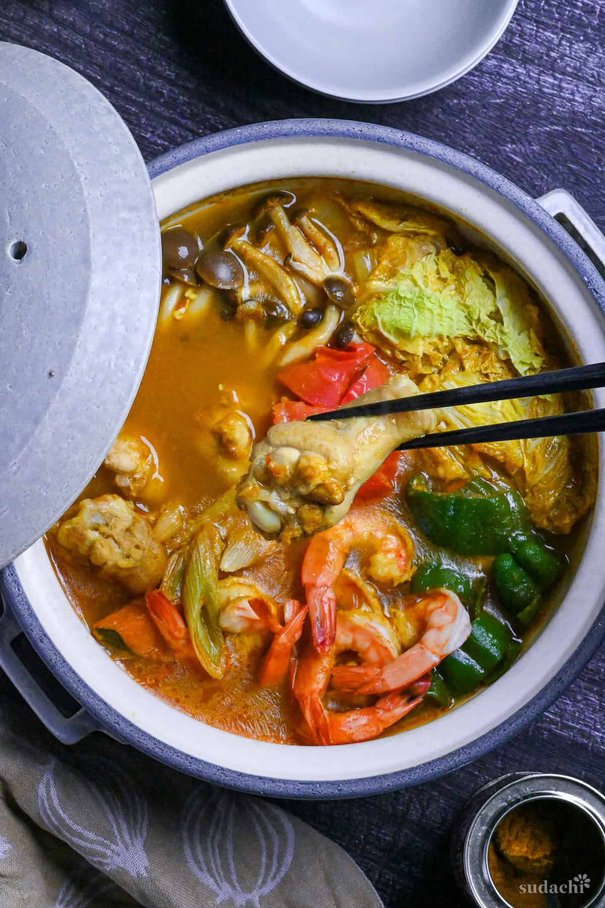 holding a chicken drumstick with black chopsticks above Japanese curry hot pot