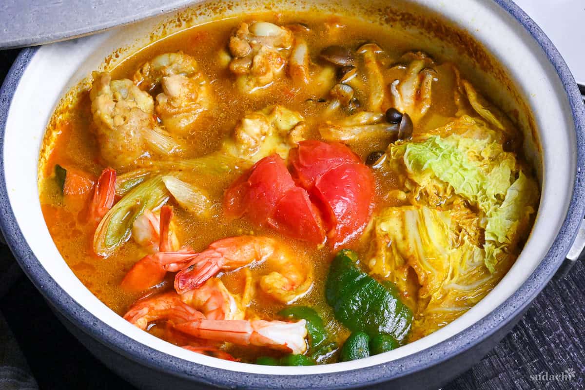 Japanese Curry Hot Pot (Kare Nabe) with chicken, prawns, vegetables and cheese in a gray ceramic pot on a black wood-effect background
