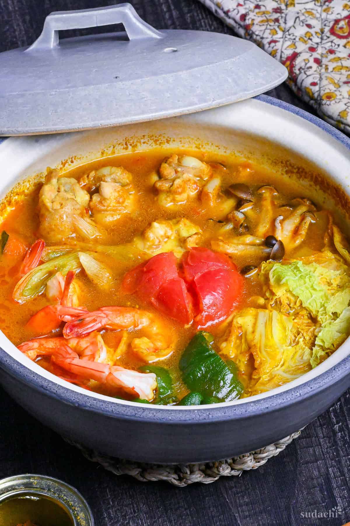 Japanese Curry Hot Pot (Kare Nabe) with chicken, prawns, vegetables and cheese in a gray ceramic pot on a black wood-effect background