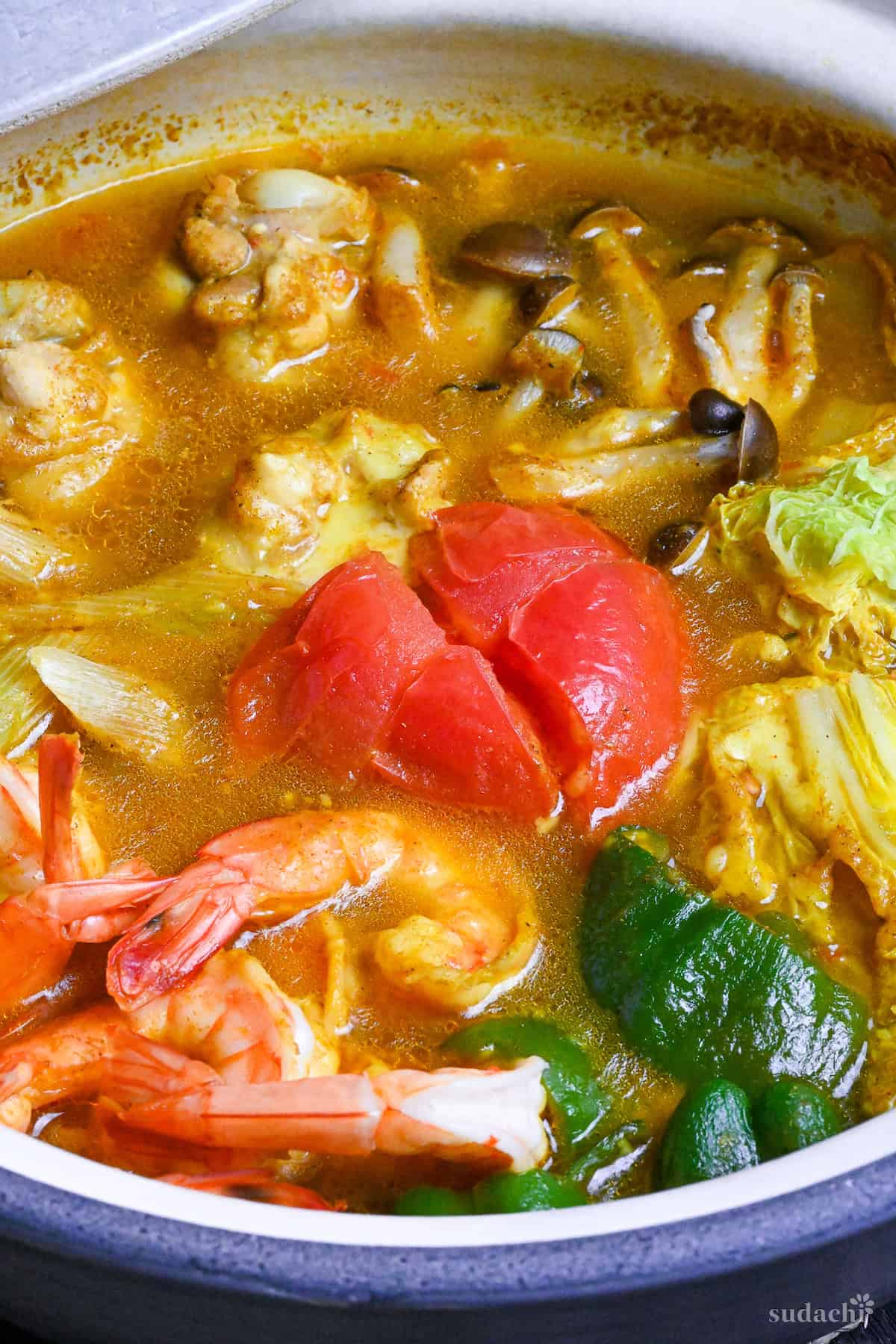 Japanese Curry Hot Pot (Kare Nabe) with chicken, prawns, vegetables and cheese in a gray ceramic pot close up