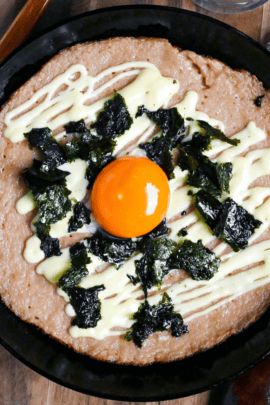 fluffy grilled grated Japanese yam topped with mayonnaise, nori and an egg yolk in a black pan on a wooden chopping board