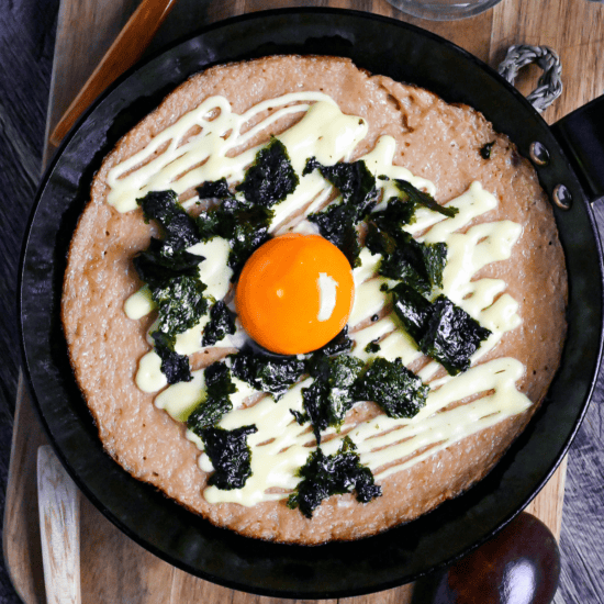 fluffy grilled grated Japanese yam topped with mayonnaise, nori and an egg yolk in a black pan on a wooden chopping board