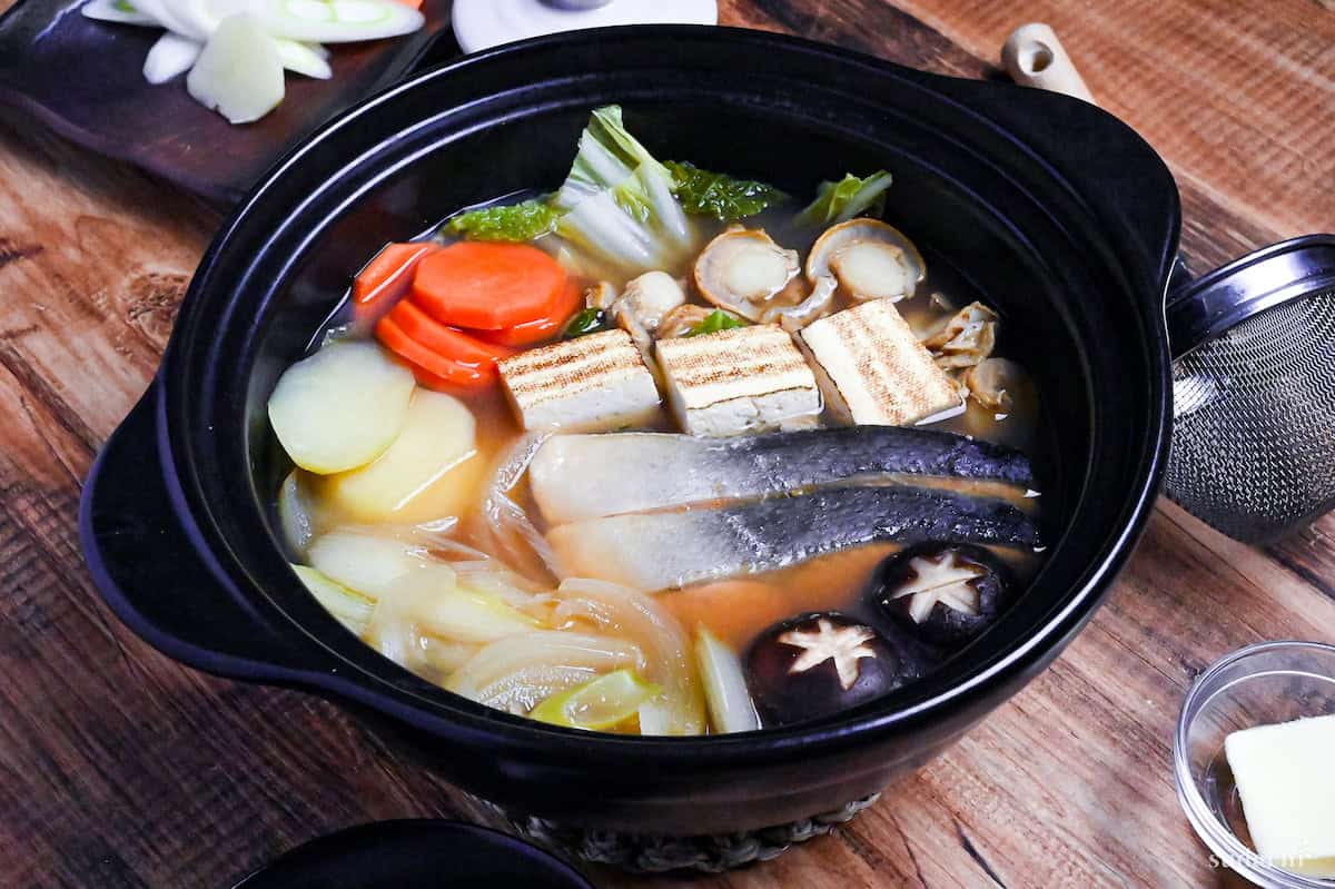Hokkaido Style Ishikari Nabe (Salmon and Miso Hot Pot) with vegetables, tofu and scallops in a black Japanese "nabe" pot on a wooden background