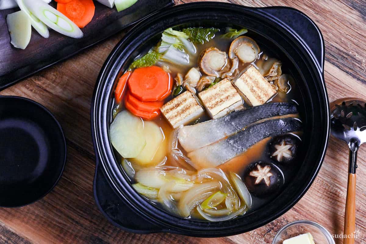 Hokkaido Style Ishikari Nabe (Salmon and Miso Hot Pot) with vegetables, tofu and scallops in a black Japanese "nabe" pot on a wooden background top down