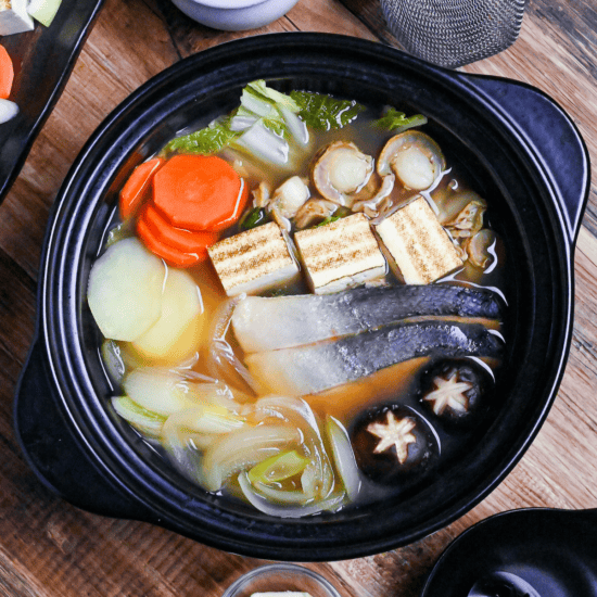 Hokkaido Style Ishikari Nabe (Salmon and Miso Hot Pot) with vegetables, tofu and scallops in a black Japanese "nabe" pot on a wooden background top down