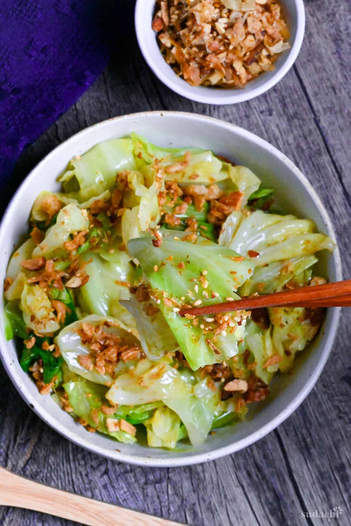 mugen cabbage in a white bowl on ashy wood surface top down view with wooden chopsticks holding one piece of cabbage