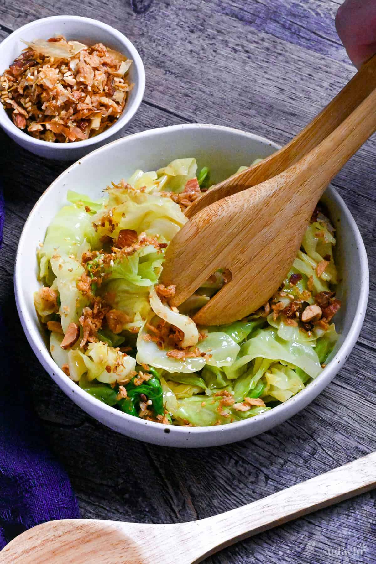 Mixing mugen cabbage in a white bowl with wooden salad tongs