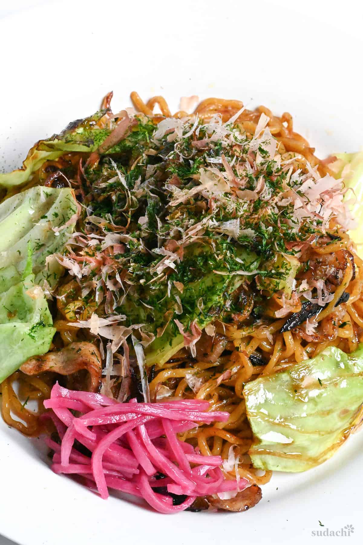 Authentic Japanese yakisoba on a white plate topped with aonori, bonito flakes and pink pickled ginger (benishoga)