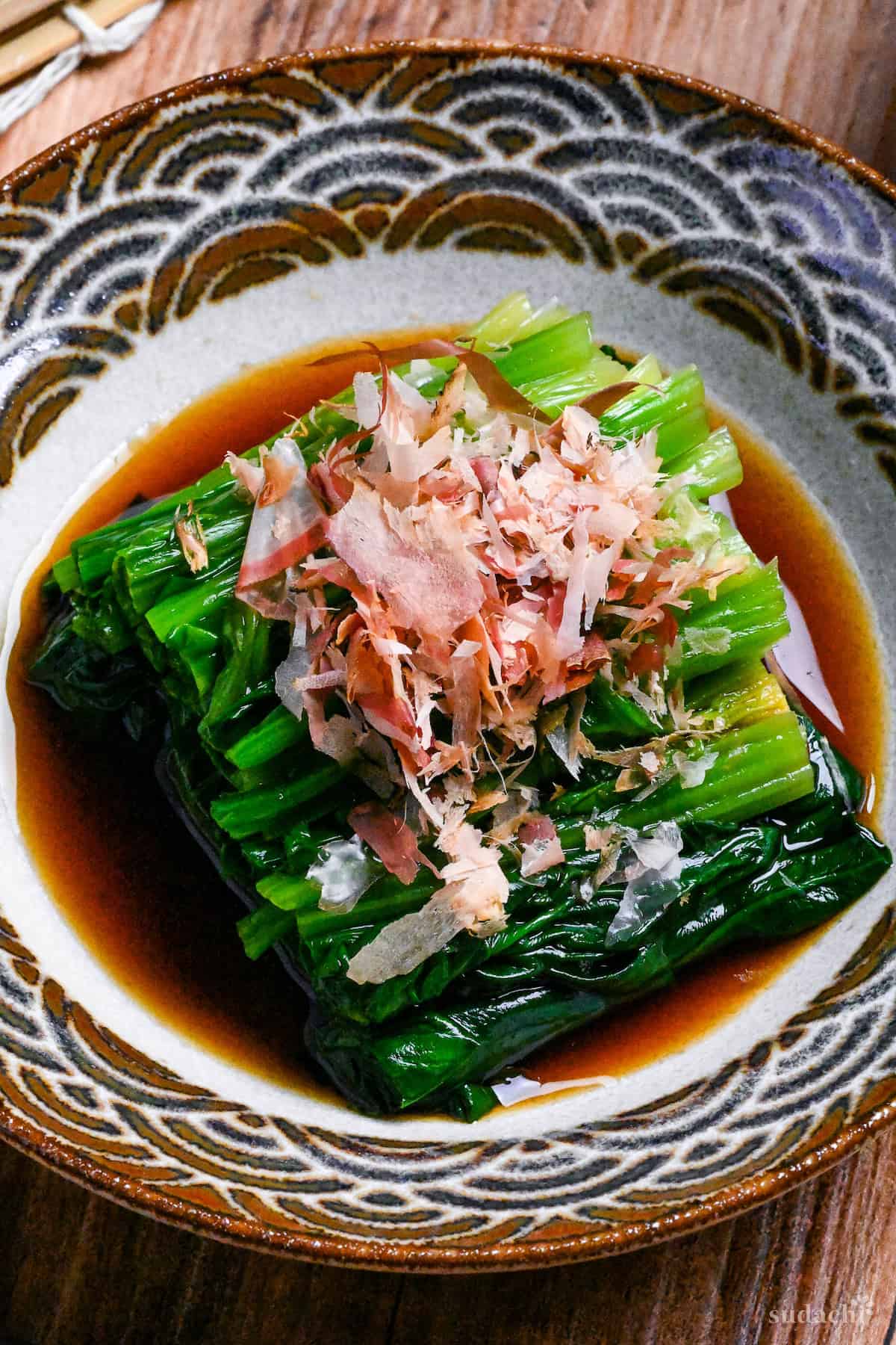 Ohitashi (Japanese spinach salad in dashi) sprinkled with bonito flakes served in a small bowl with brown and gray seigaiha pattern around the edge