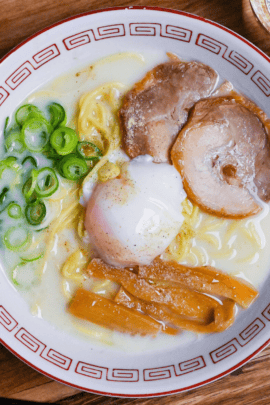 Sugakiya Ramen Copycat recipe topped with chashu, menma bamboo shoots, chopped green onions and an onsen (hot spring) egg served in a white and red ramen bowl