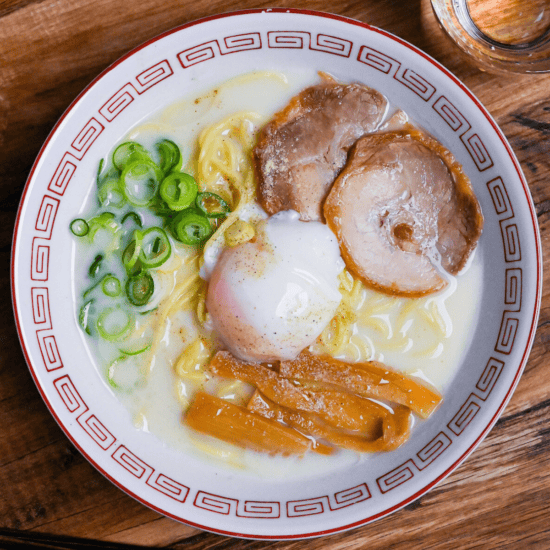 Sugakiya Ramen Copycat recipe topped with chashu, menma bamboo shoots, chopped green onions and an onsen (hot spring) egg served in a white and red ramen bowl