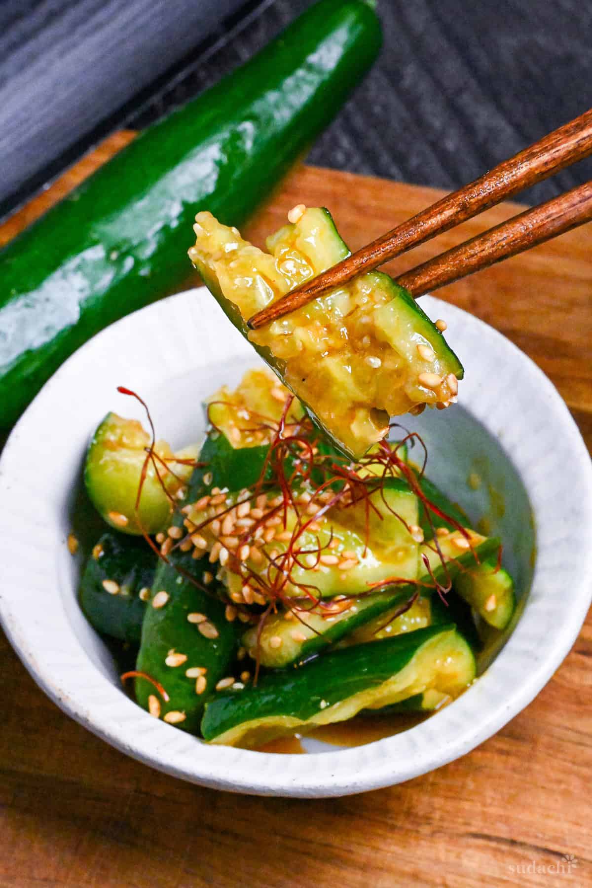 Close up of Japanese smashed cucumber (tataki kyuri) coated in spicy miso sauce held up with wooden chopsticks