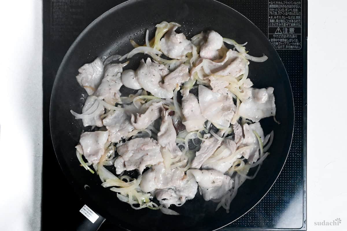 Thinly sliced pork belly and onions frying in a pan on the stove