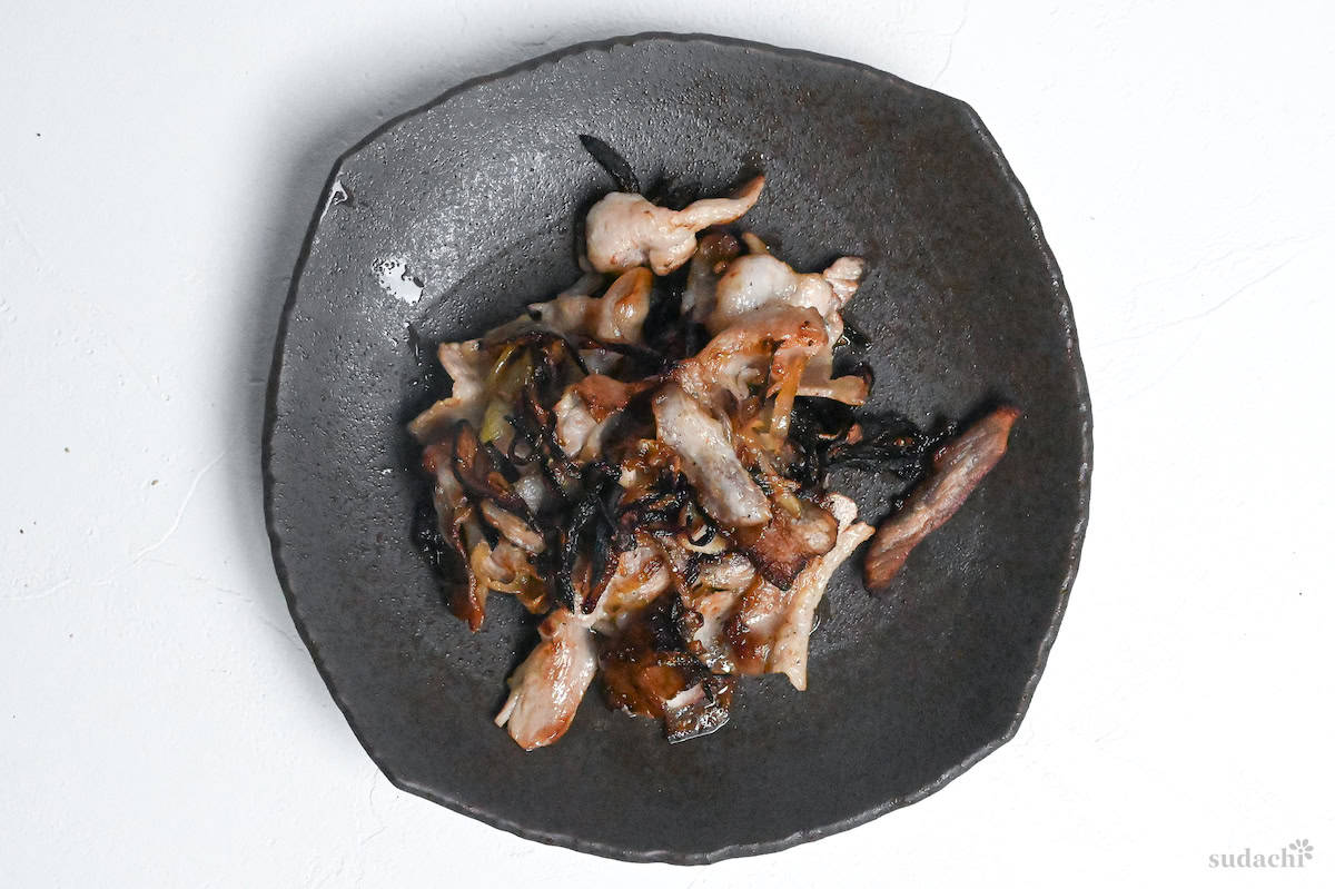 pan-fried thinly sliced pork belly and onions on a brown plate on a white background