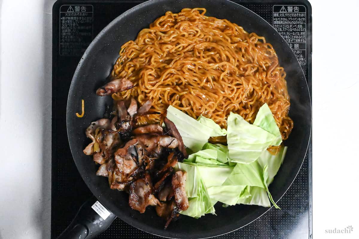 yakisoba noodles, thinly sliced pork, onions and cabbage in a frying pan on the stove