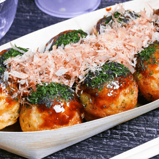 8 crispy gindako style takoyaki topped with glossy brown sauce, aonori and bonito flakes on a black wood-effect background