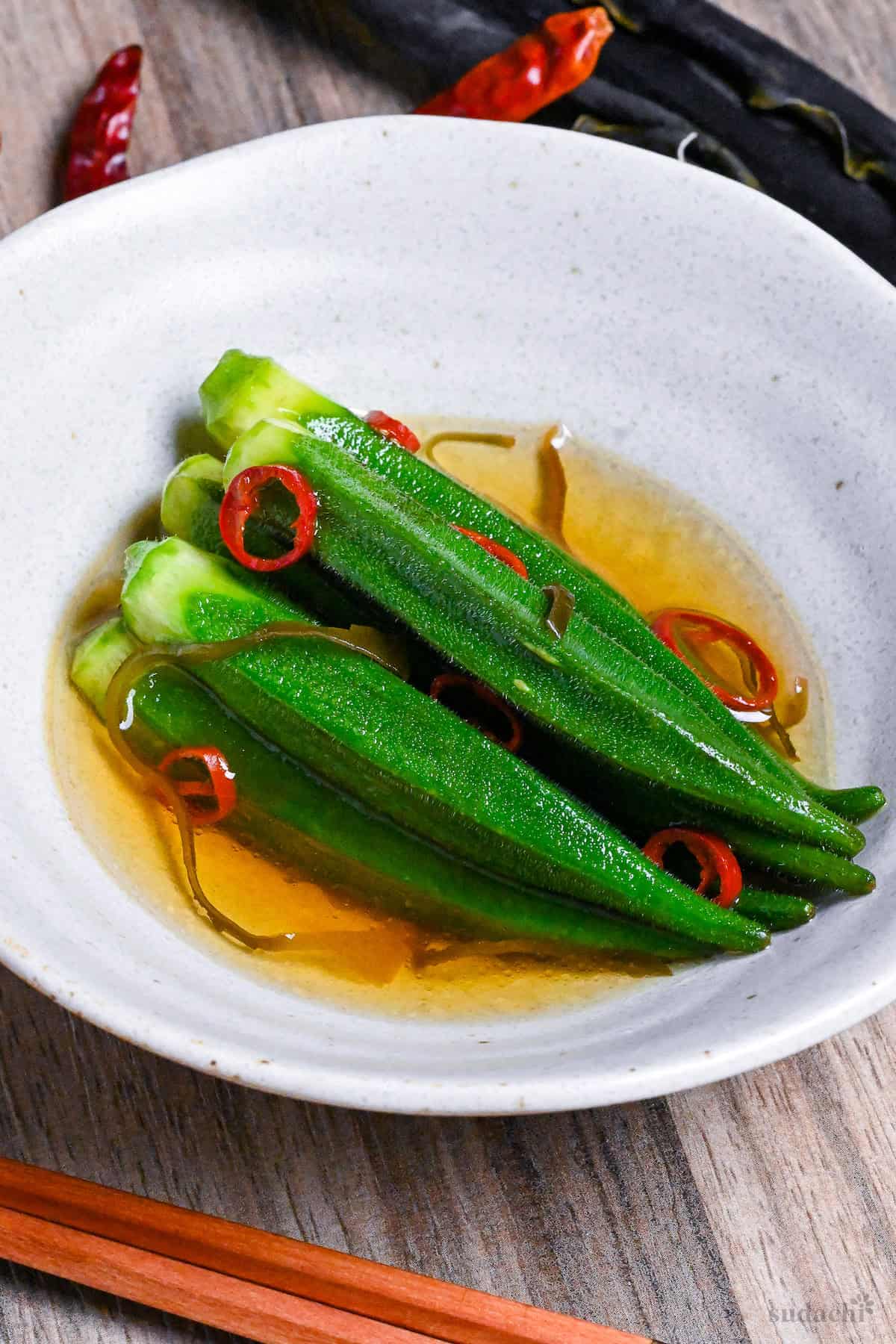 shio okra in a white bowl with chili and shio kombu on an ashy wooden background