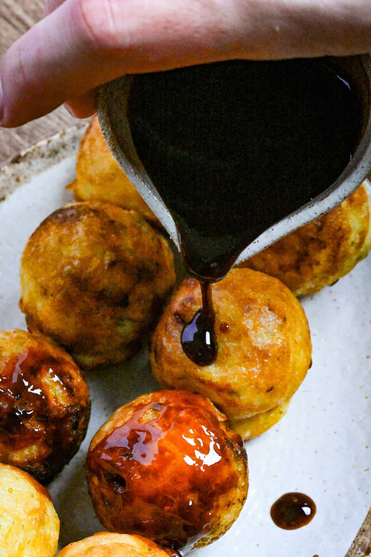 Pouring homemade takoyaki sauce over takoyaki on a white and brown plate