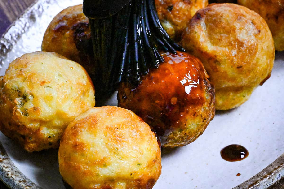 Brushing takoyaki with homemade takoyaki sauce using a black silicone pastry brush