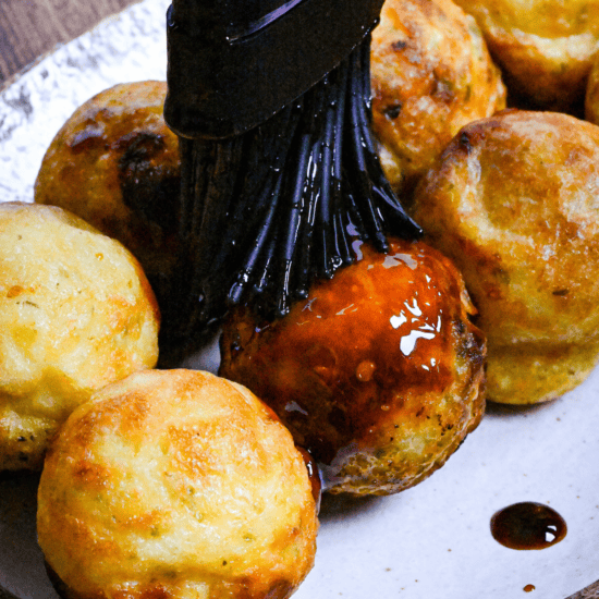 Brushing takoyaki with homemade takoyaki sauce using a black silicone pastry brush