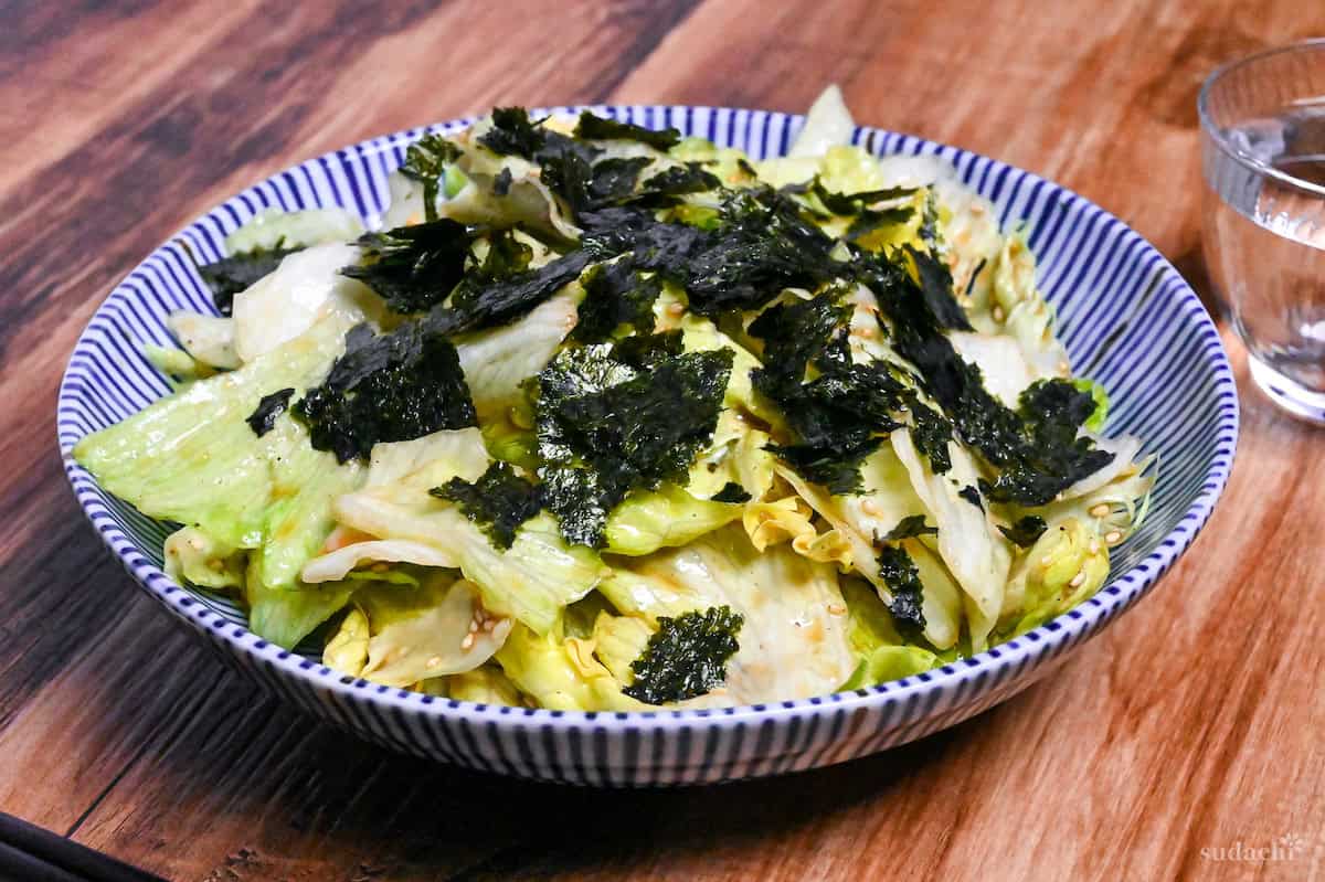 Yamitsuki lettuce topped with roughly torn nori in a white bowl with blue stripes on a wooden background