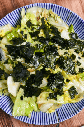 Yamitsuki lettuce topped with roughly torn nori in a white bowl with blue stripes on a wooden background top down