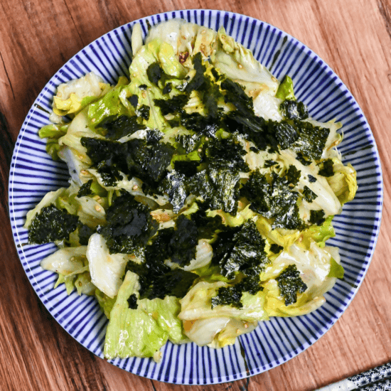 Yamitsuki lettuce topped with roughly torn nori in a white bowl with blue stripes on a wooden background top down