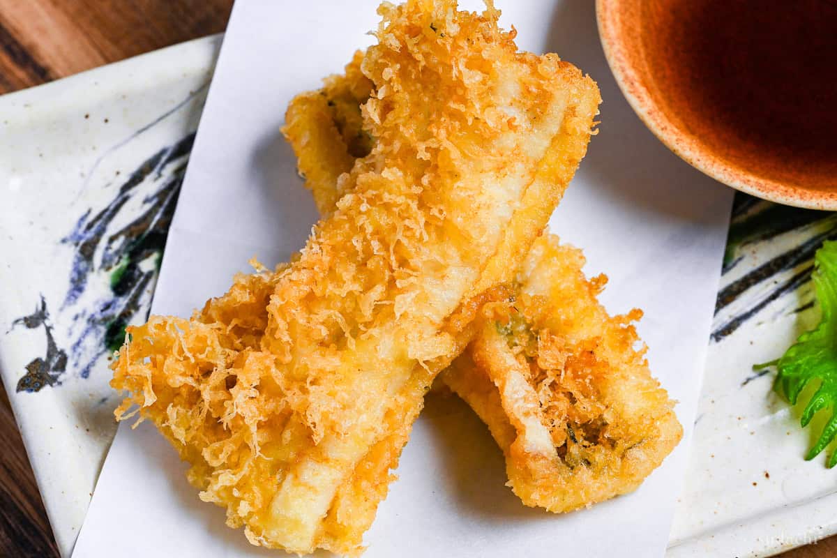 two pieces of conger eel tempura on a rectangular plate with tempura dipping sauce and grated daikon on a perilla leaf
