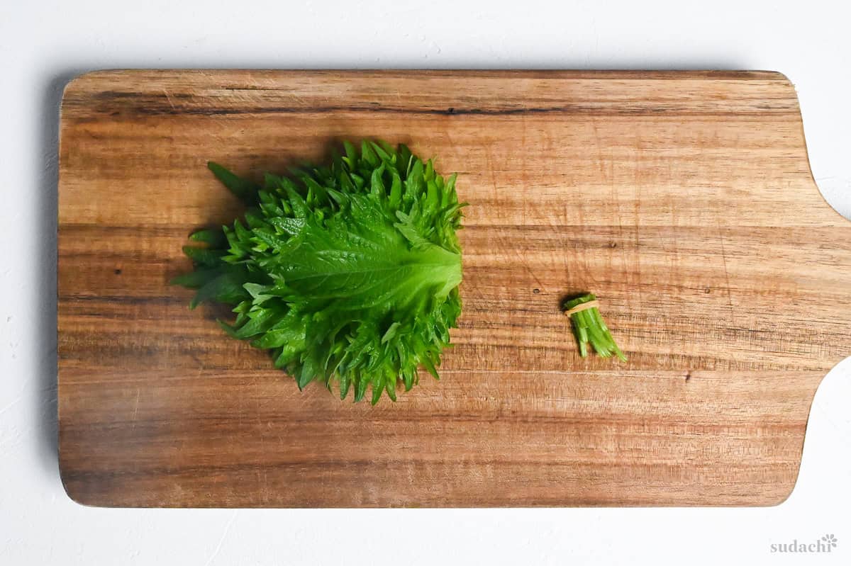 Ooba leaves with the stems cut off on a wooden chopping board on a white background