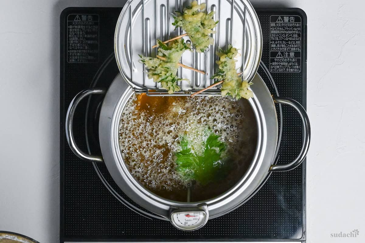 shiso Perilla leaf with one side coated with tempura batter frying in a pot of oil