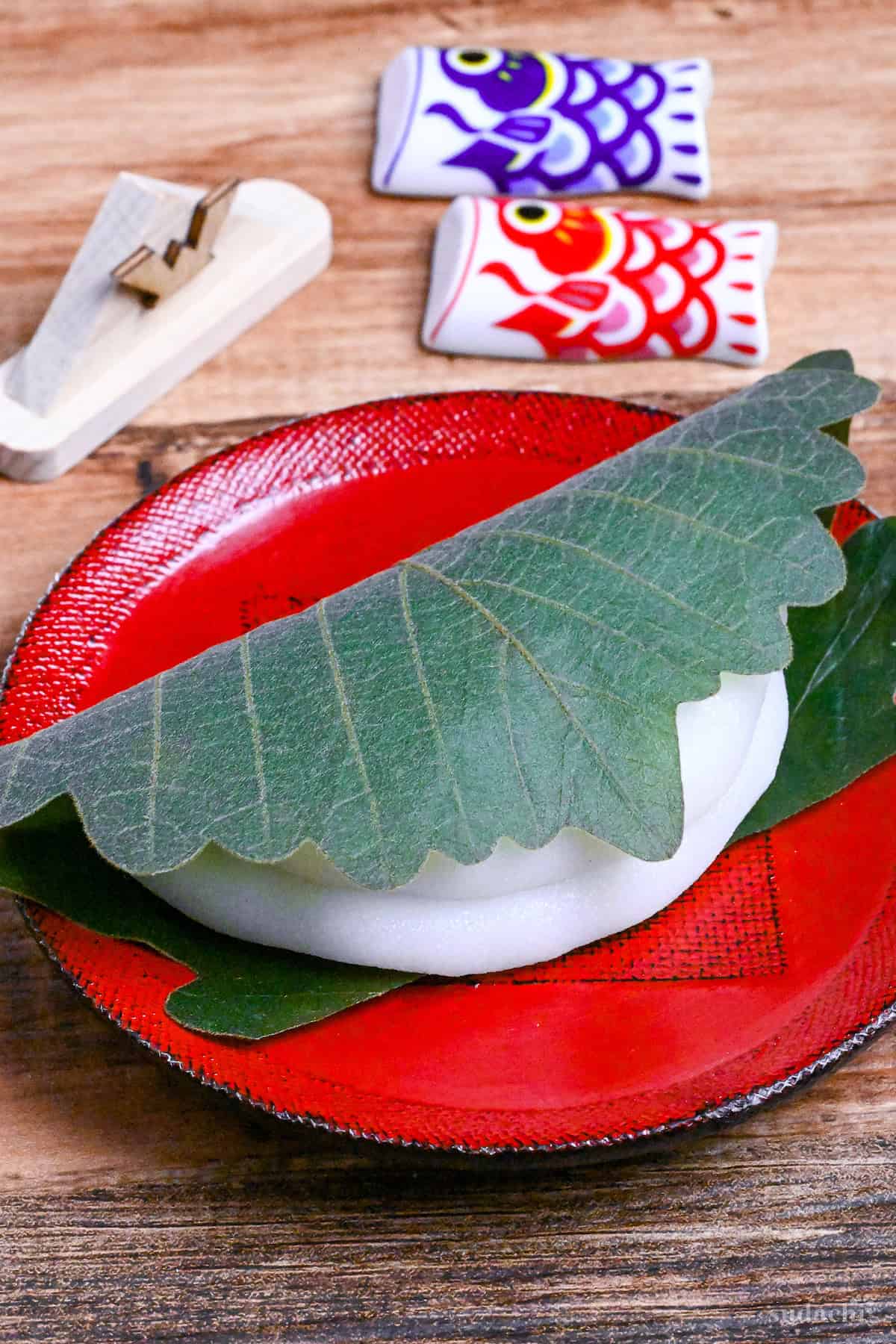 one kashiwa mochi wrapped with an oak leaf on a red plate on a wooden background