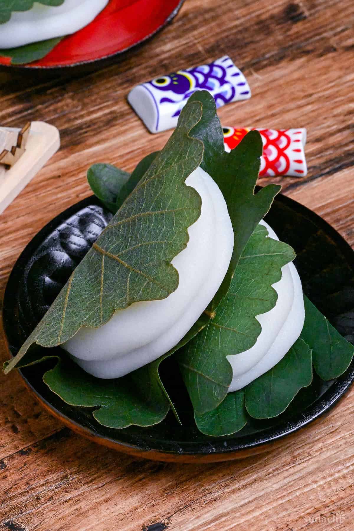 two kashiwa mochi wrapped with oak leaves on a black wooden plate on a wooden background