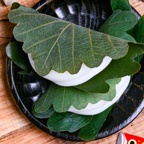 two kashiwa mochi wrapped with oak leaves on a black wooden plate on a wooden background