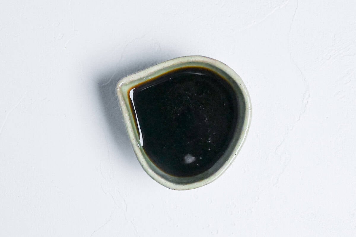 Homemade kuromitsu (Japanese dark sugar syrup) in a small green ceramic jug with it drizzled over mochi in the background