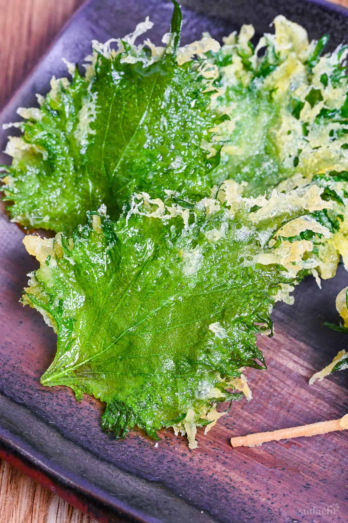 Three flat ooba (shiso) tempura made with Perilla leaves on a brown/purple plate on a wooden background close up