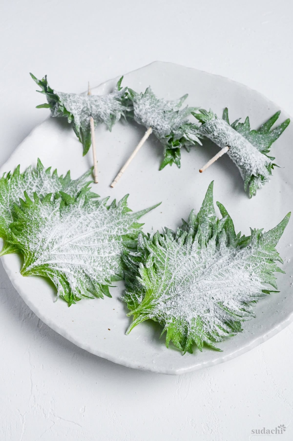 Ooba leaves coated with flour to help tempura batter stick on a white plate on a white background