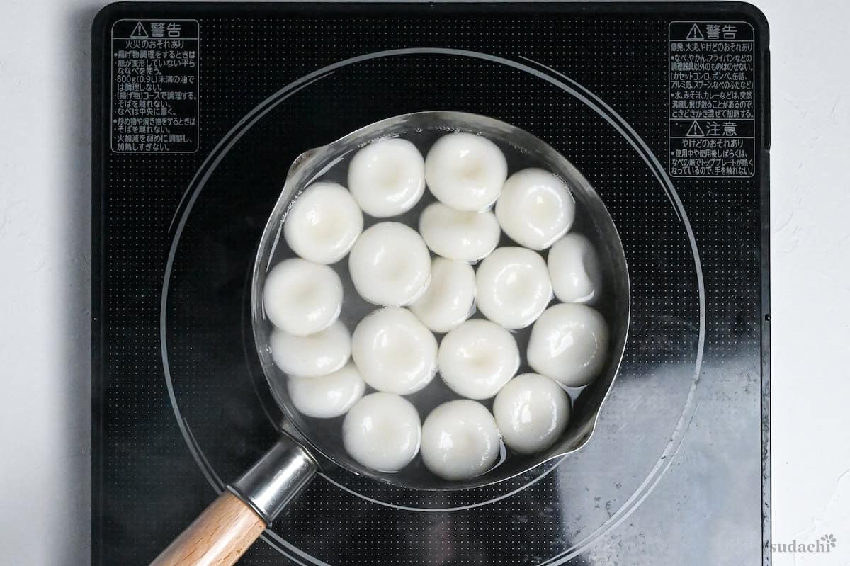 shiratama dango floating in boiling water in a pot on the stove top