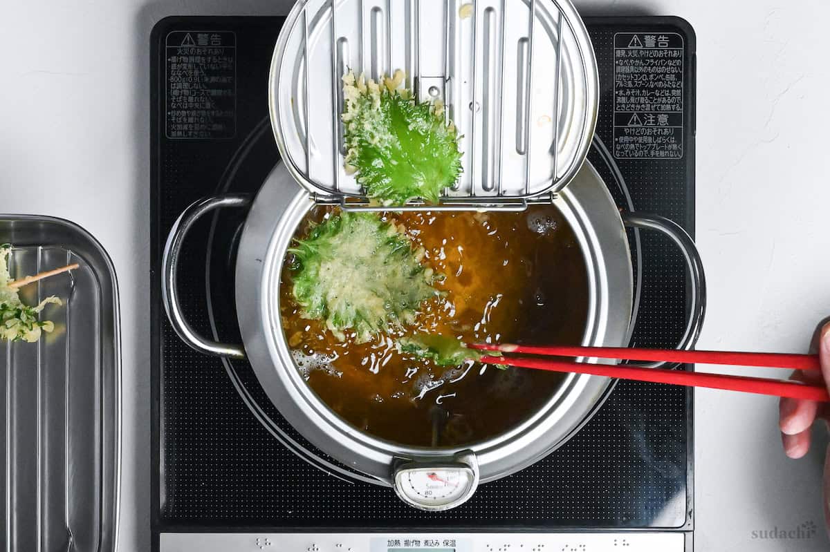 removing ooba tempura from pot of oil using red cooking chopsticks