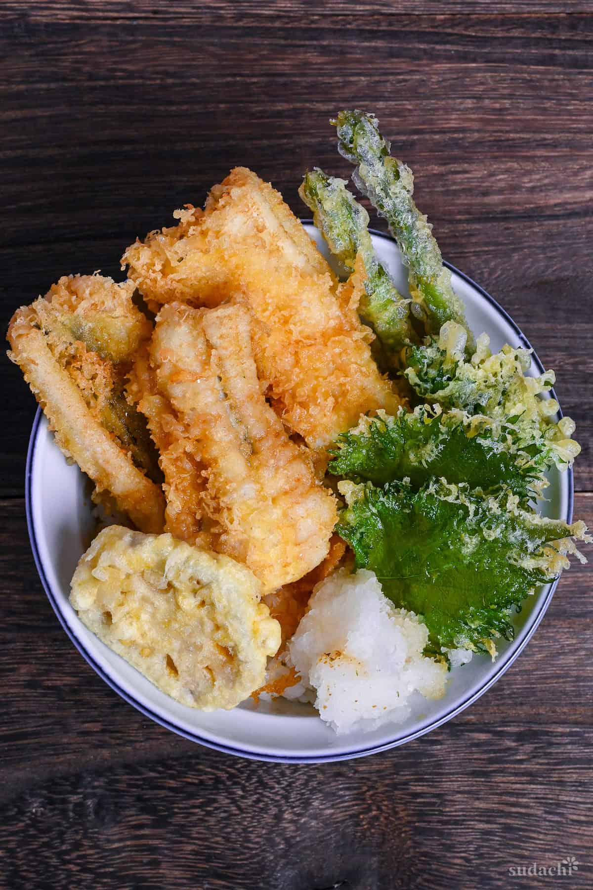 Tendon (Tempura rice bowl) made with conger eel, renkon, asparagus, shiso leaves and grated daikon over rice in a blue bowl