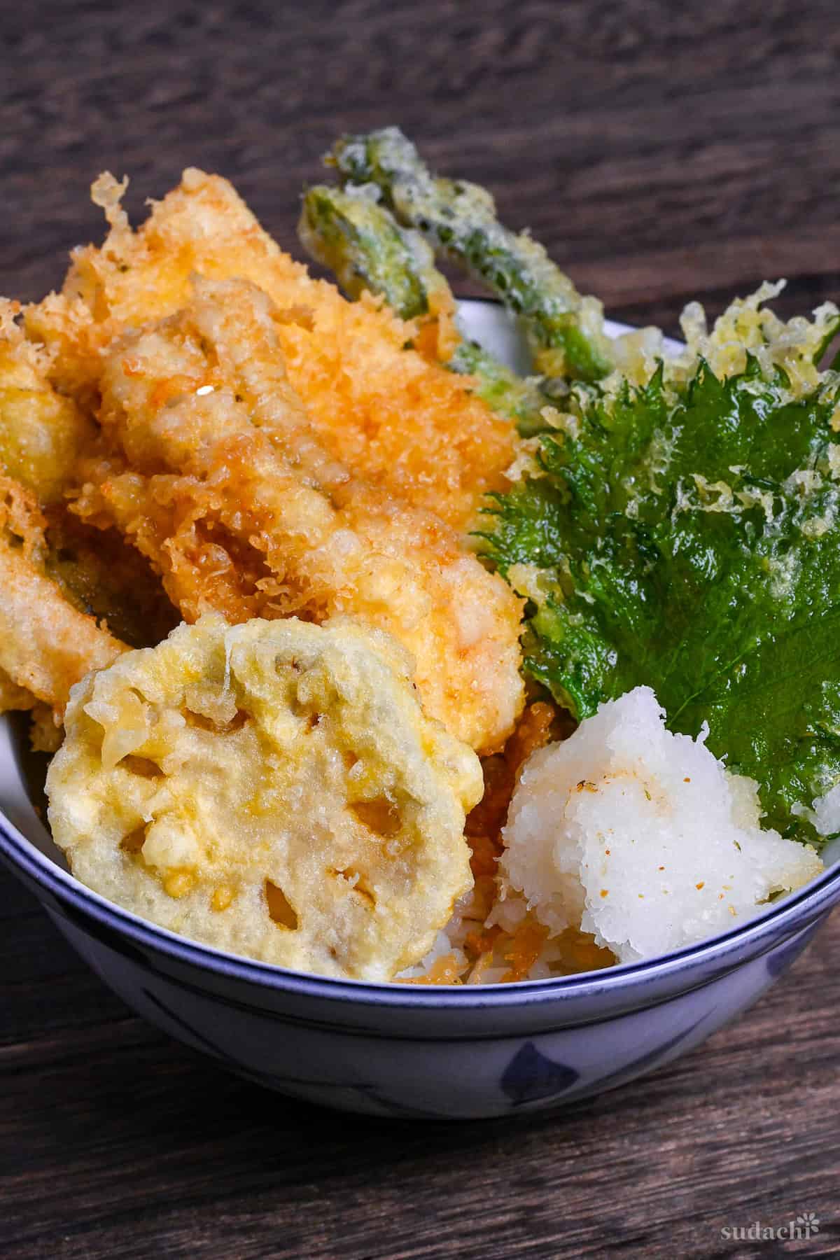 Tendon (Tempura rice bowl) made with conger eel, renkon, asparagus, shiso leaves and grated daikon over rice in a blue bowl