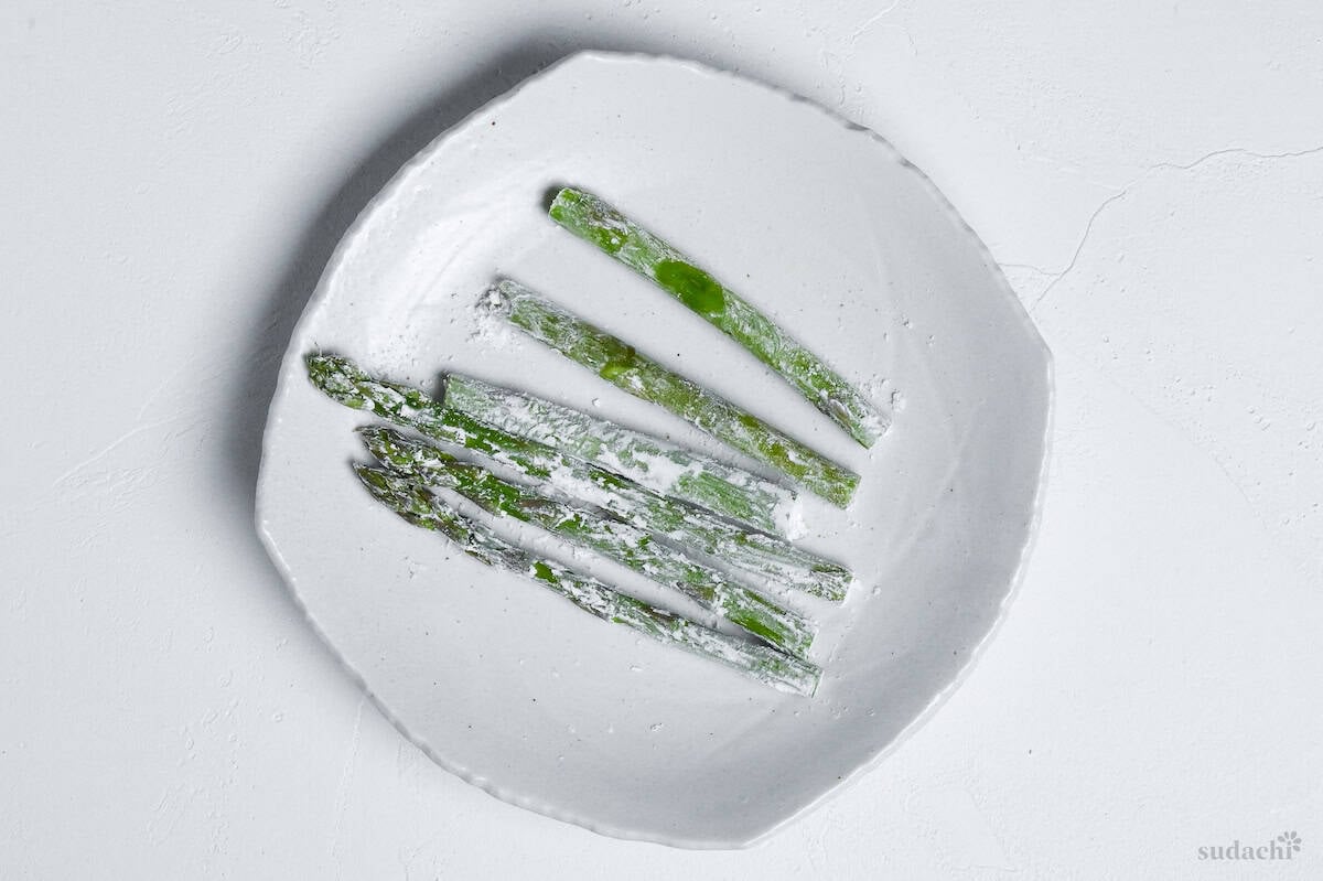 6 pieces of asparagus coated with flour on a white plate
