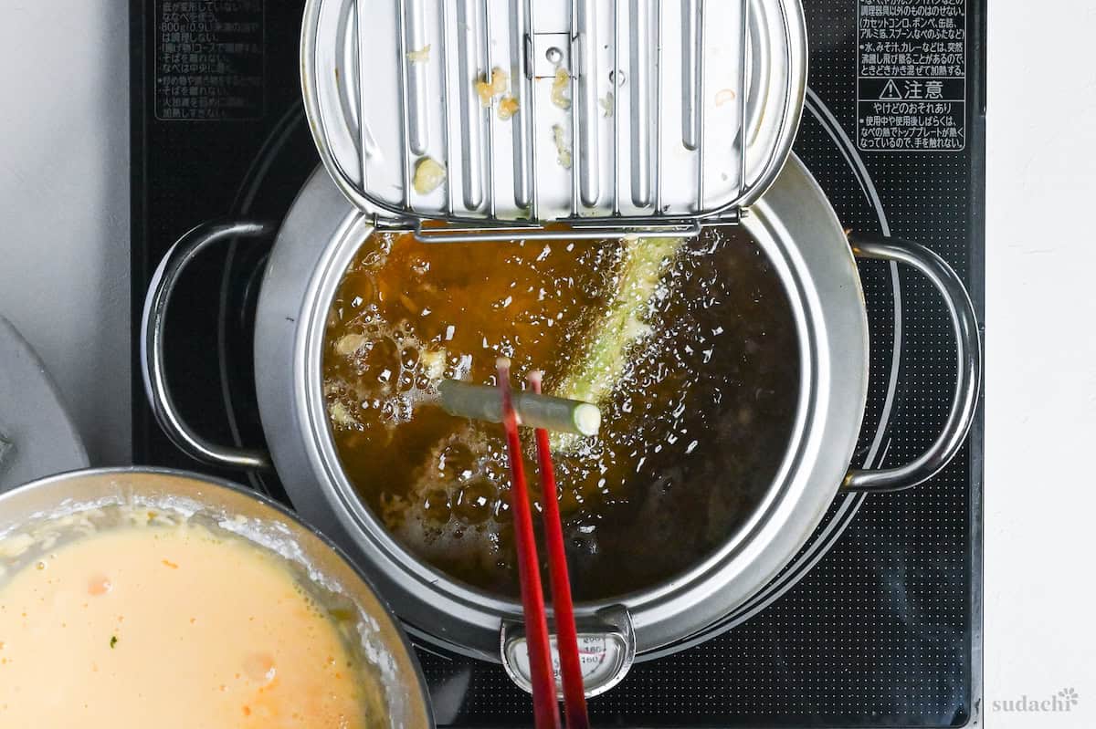 dipping flour-coated asparagus into tempura batter and then into hot oil in a Japanese-style tempura frying pot