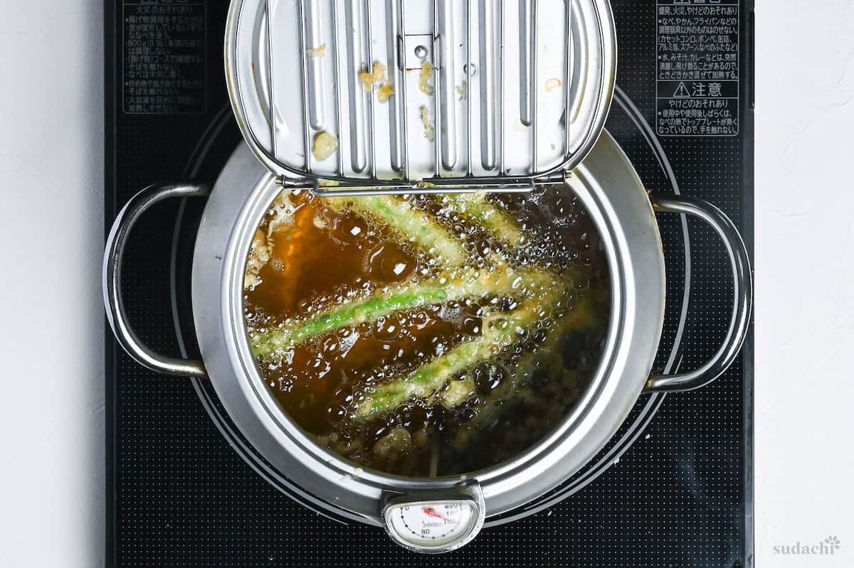 Asparagus tempura frying in a Japanese-style tempura frying pot