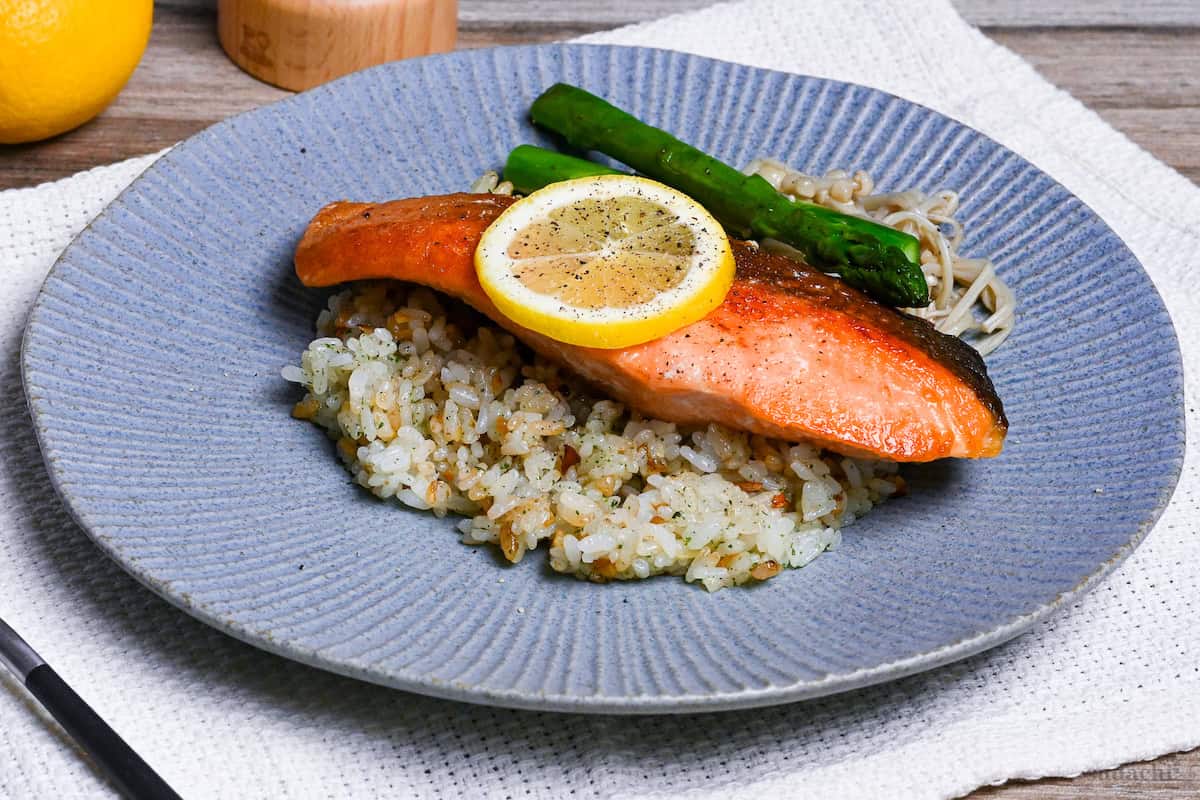 Butter Soy Sauce Salmon (Japanese-Style Salmon Meunière) on a bed of garlic rice next to sautéed asparagus and enoki mushrooms on a blue striped dinner plate side view