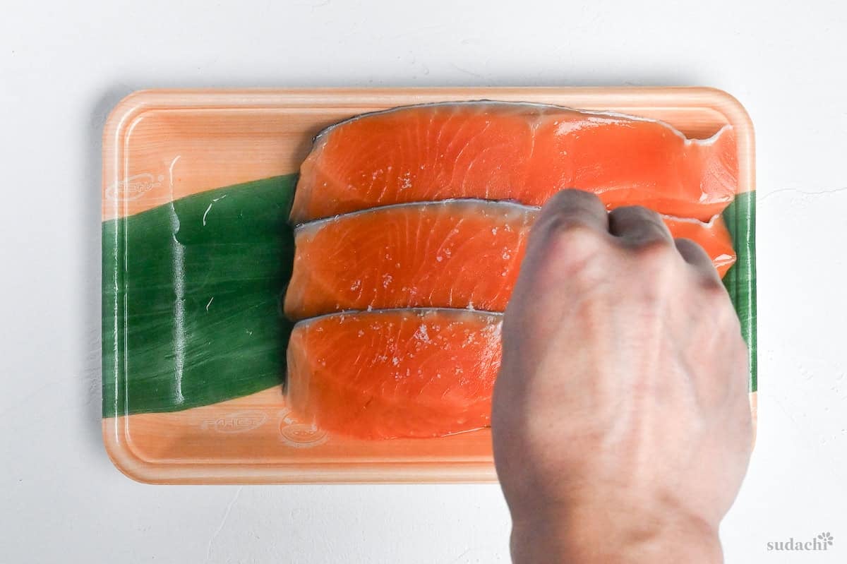 sprinkling salt over three fresh salmon fillets