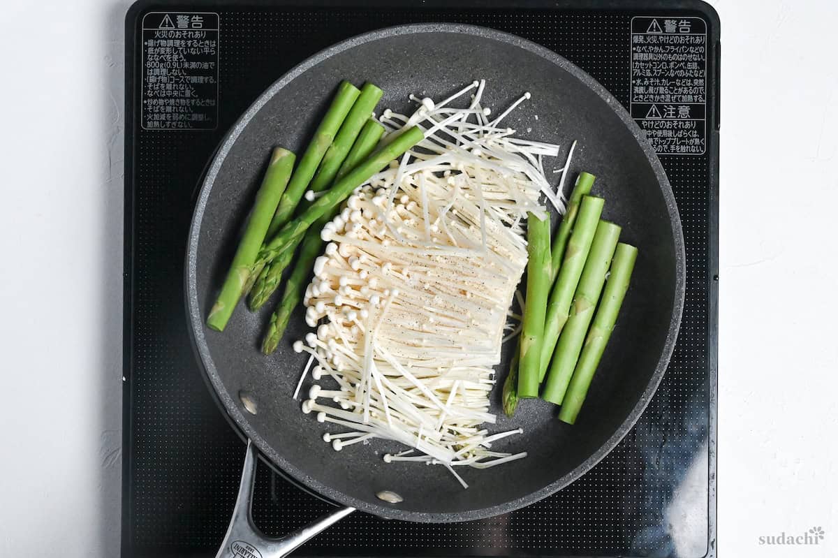 Asparagus and enoki mushrooms sprinkled with salt and pepper in a frying pan