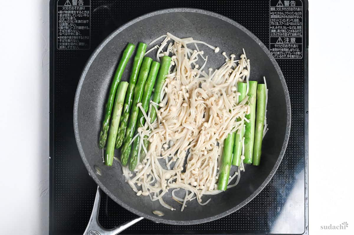 softened enoki mushrooms in a pan with asparagus
